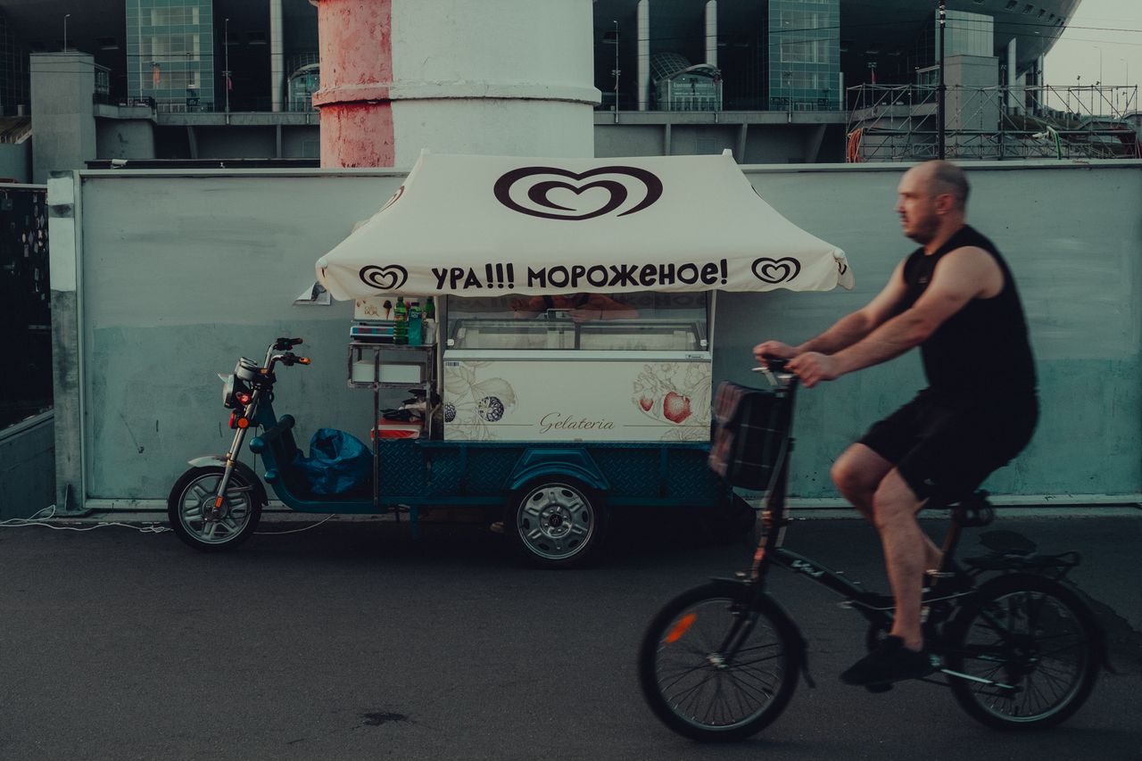 A man cycling past an ice cream cart on a street in Saint Petersburg, Russia.